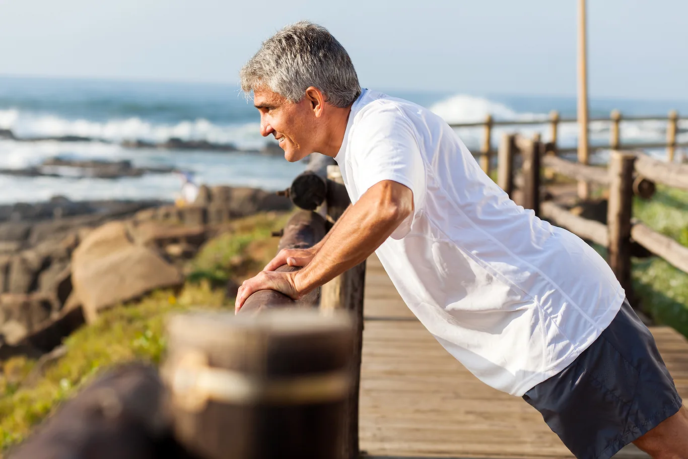 Man with grey hair stretching by the sea
